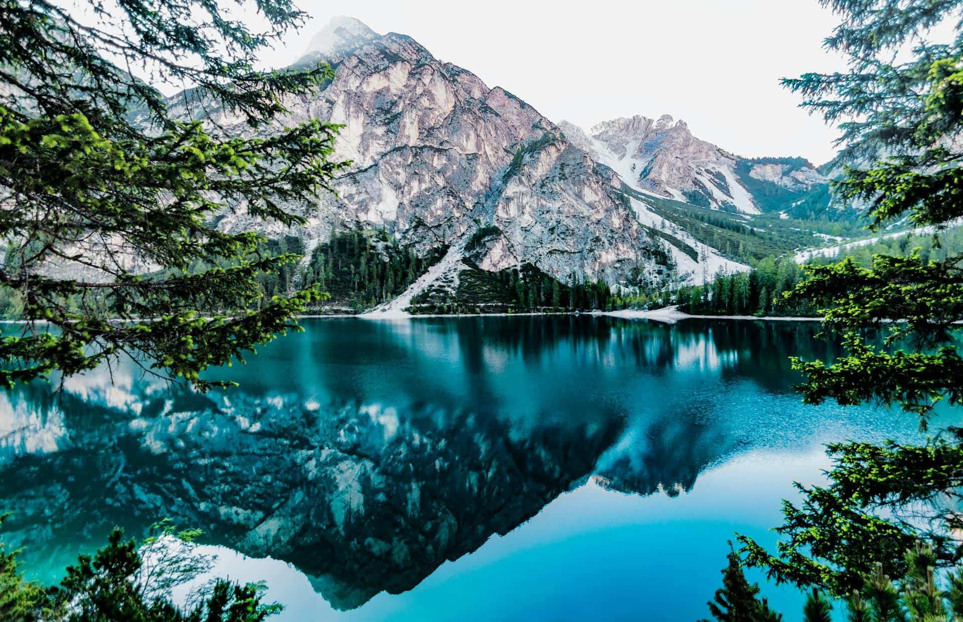 An alpine lake reflecting rocky, snow dusted peaks and conifer forest